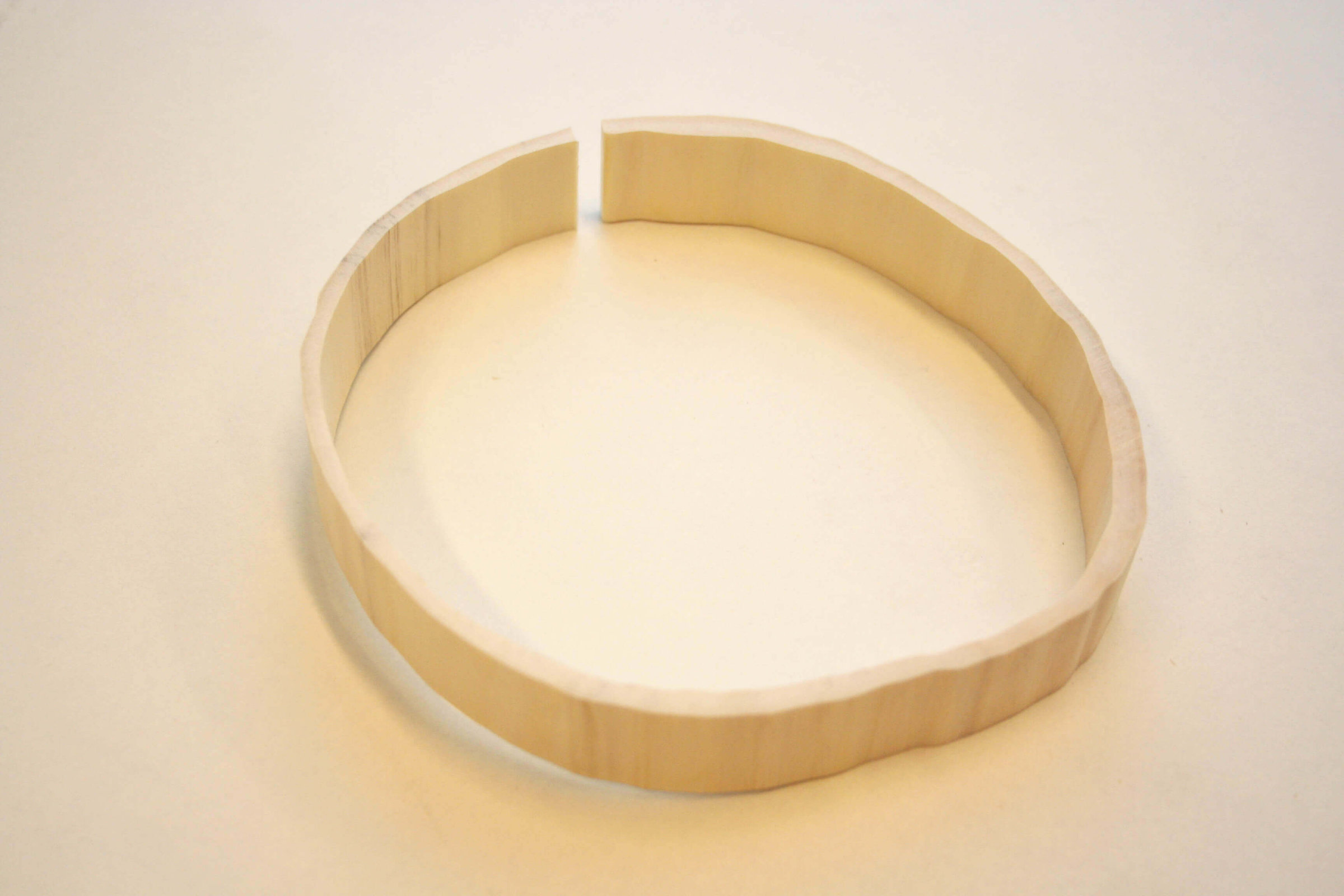 Wooden ring sculpture made from a tree growth ring, circular form with an opening, photographed on a neutral background.
