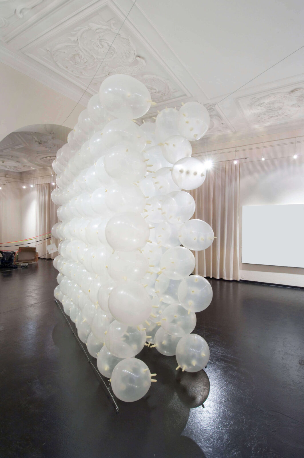 Installation view of a structure made of inflated white latex gloves forming a corridor in an exhibition space.