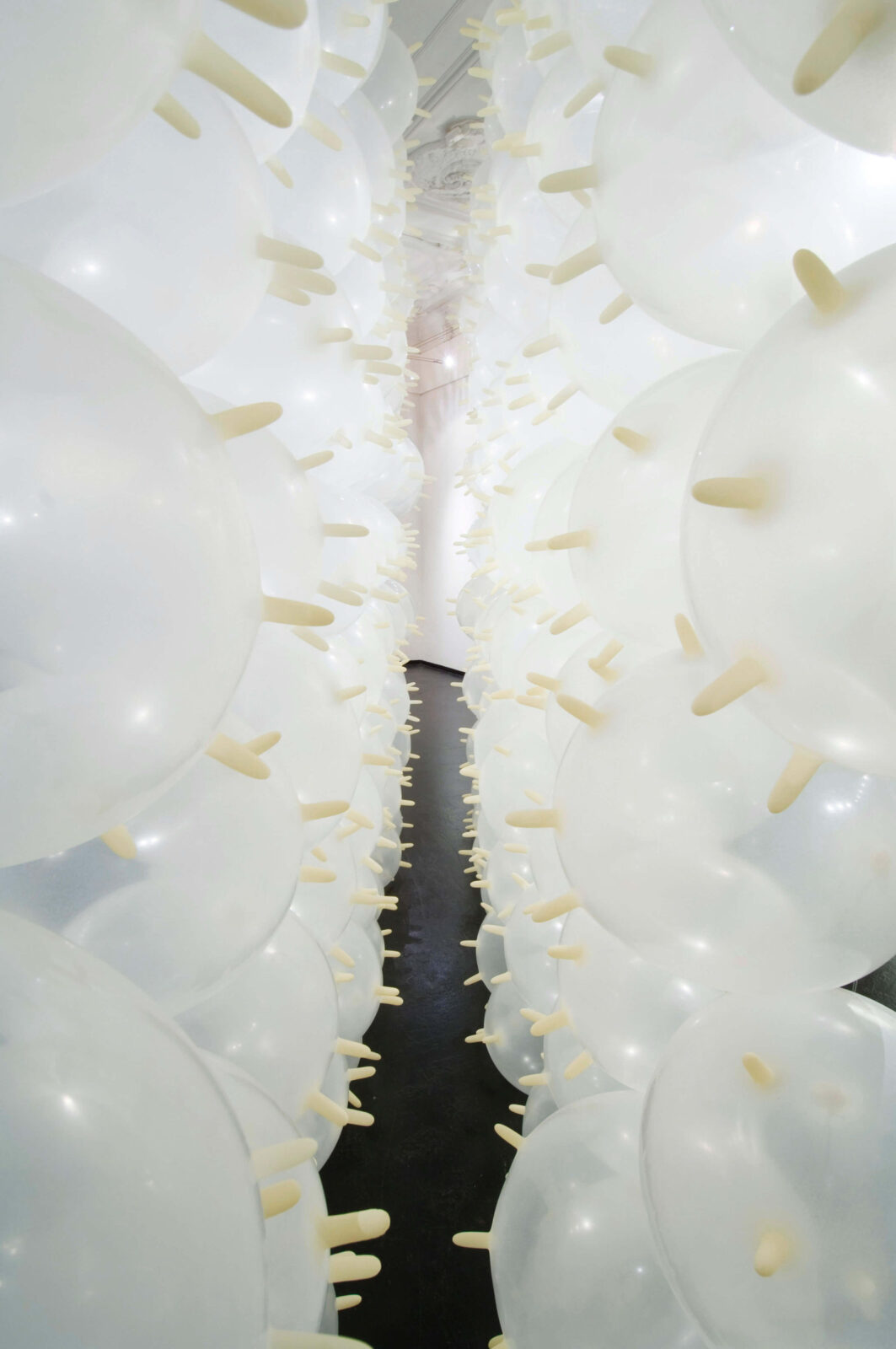 Interior view of an installation composed of inflated white latex gloves forming a narrow passage.