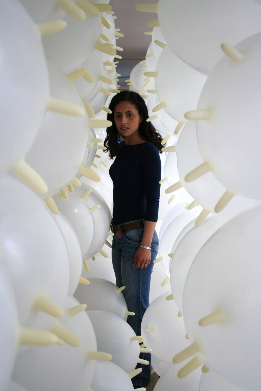 Person standing inside an installation made of inflated white latex gloves arranged as a walkable corridor.