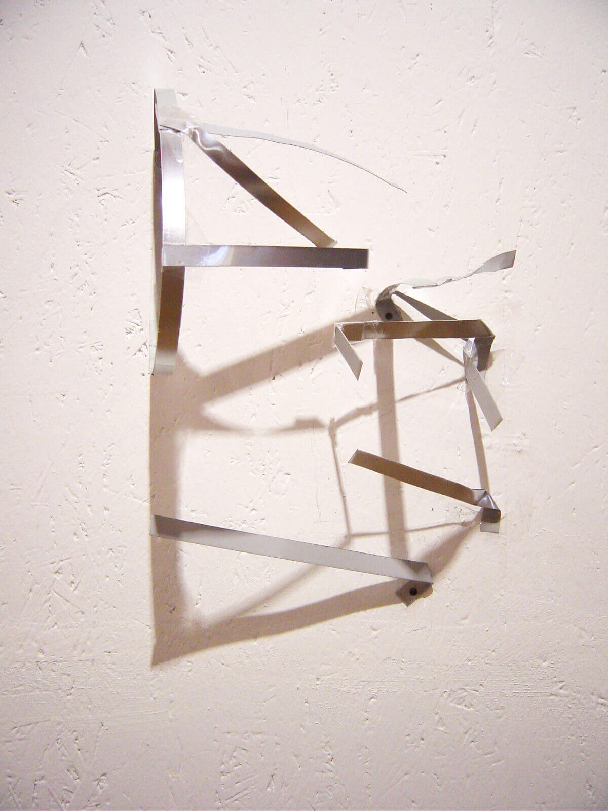 Abstract wall installation composed of folded metal strips forming angular shapes and shadows.