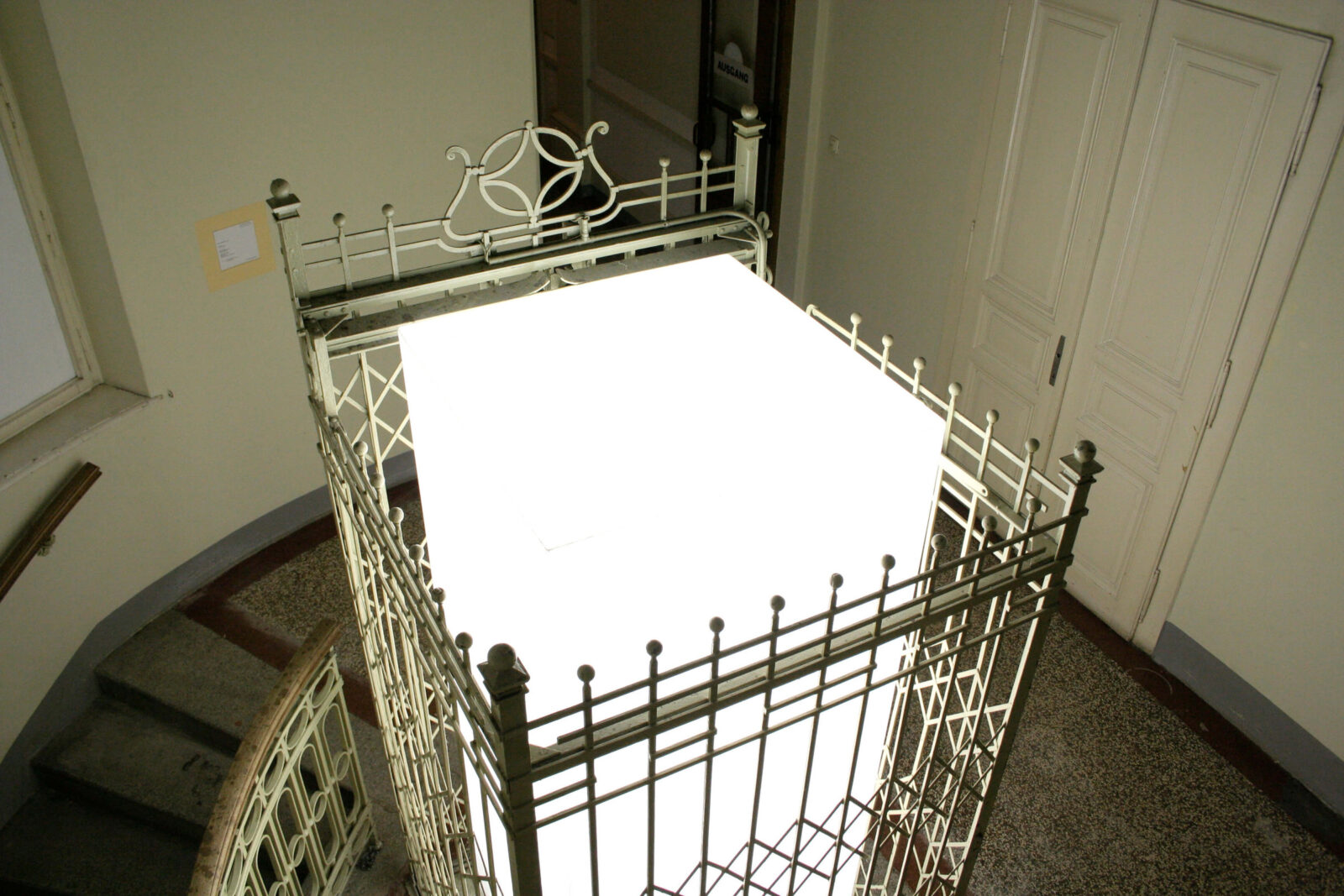 Top view of a glowing cubic installation positioned within an architectural metal structure.