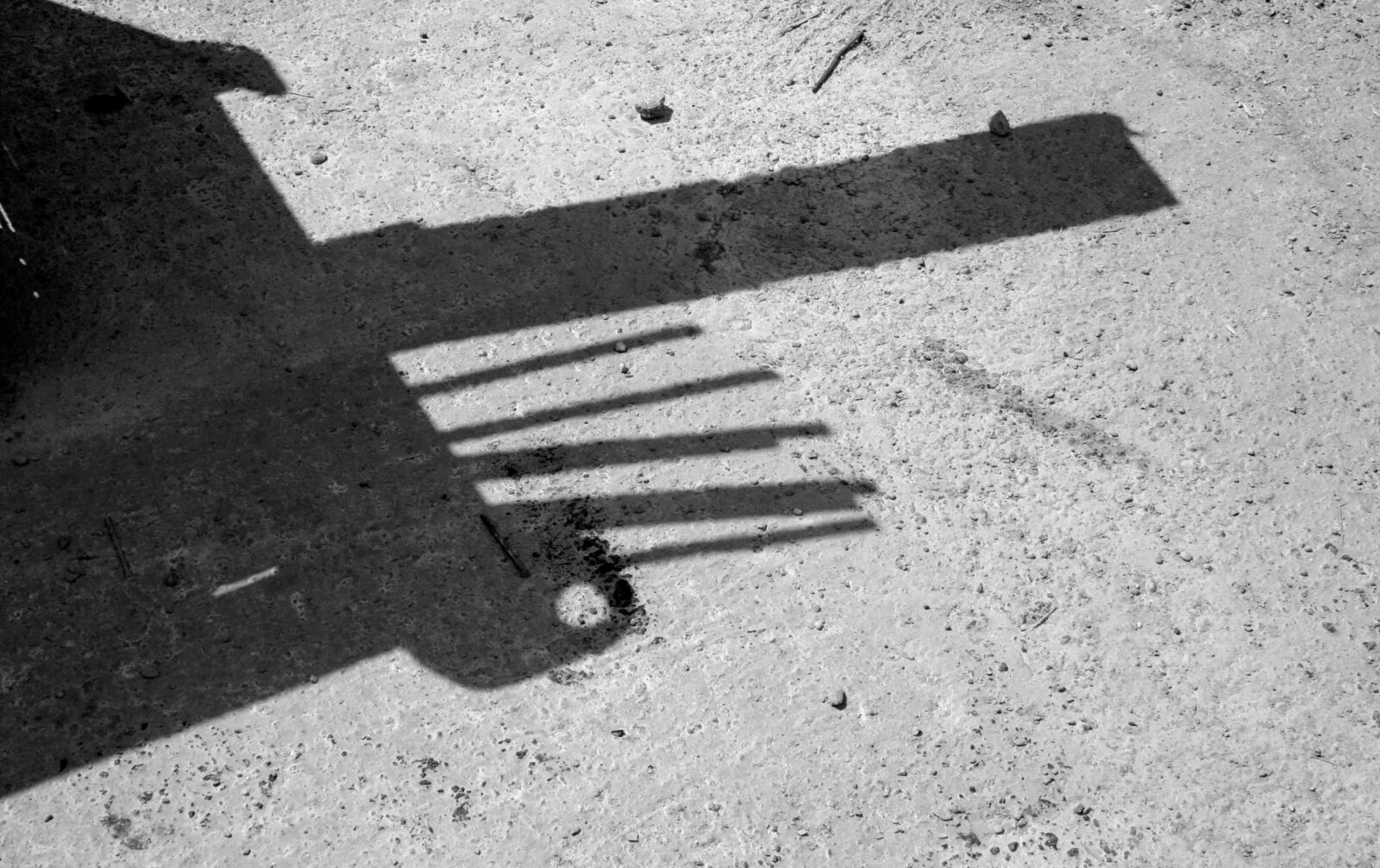 Shadow of elongated linear elements projected onto a concrete surface in monochrome.