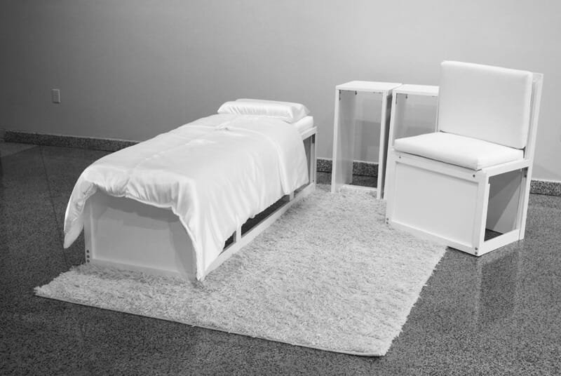 Transformable object assembled into a bed, chair, and side tables made of white modular elements displayed on a white rug.