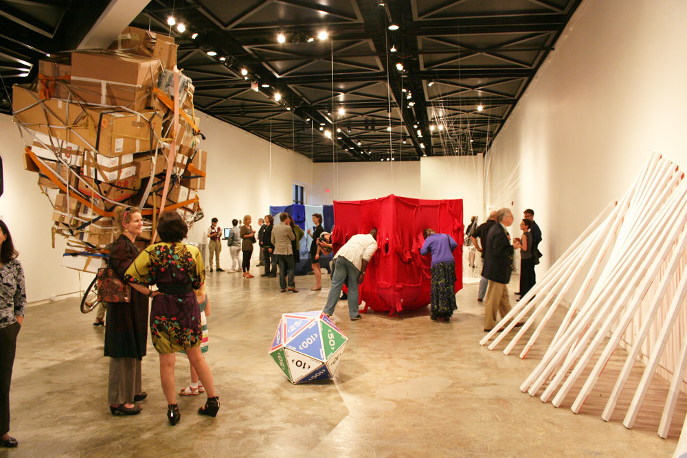 Exhibition view showing multiple large-scale installations, including textile-covered cubic structures and sculptural objects in a gallery space with visitors.